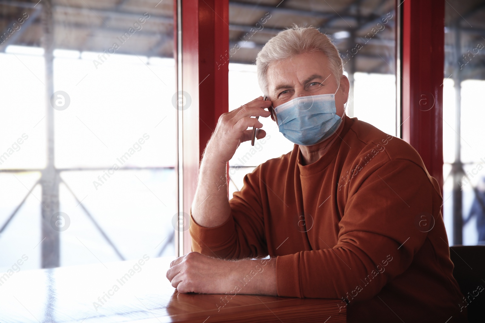 Photo of Senior man with medical mask talking on mobile phone in cafe. Virus protection