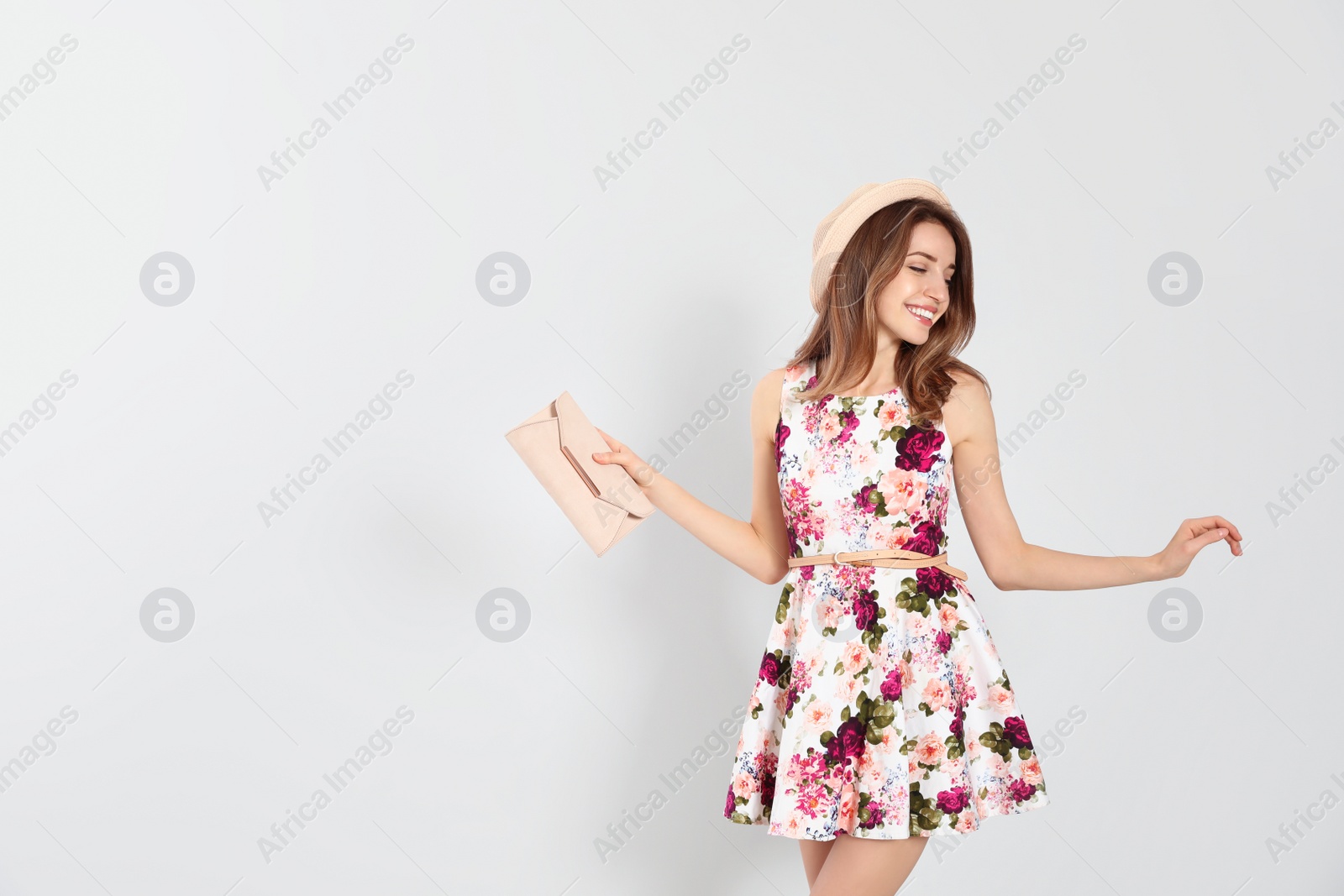 Photo of Young woman wearing floral print dress with clutch on light background. Space for text