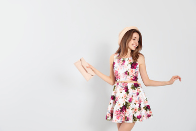 Young woman wearing floral print dress with clutch on light background. Space for text