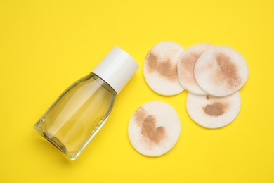 Photo of Bottle of makeup remover and dirty cotton pads on yellow background, flat lay