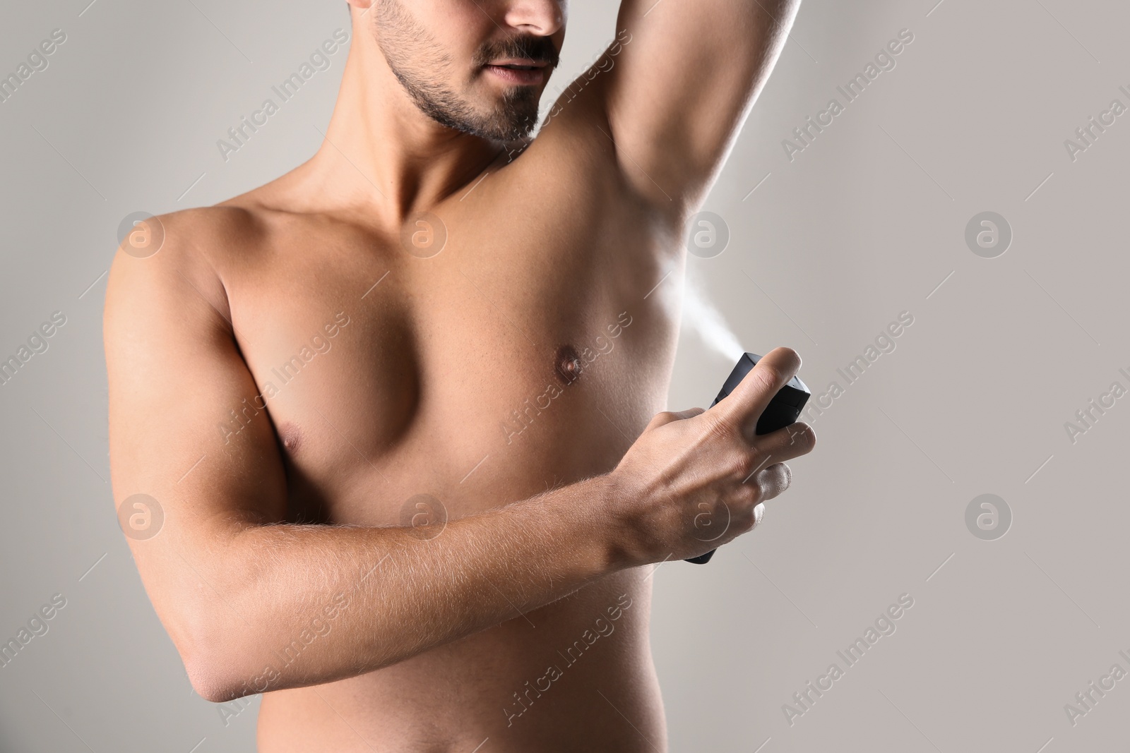 Photo of Young man using deodorant on gray background, closeup