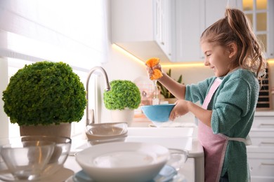Photo of Little girl washing dishes in kitchen at home
