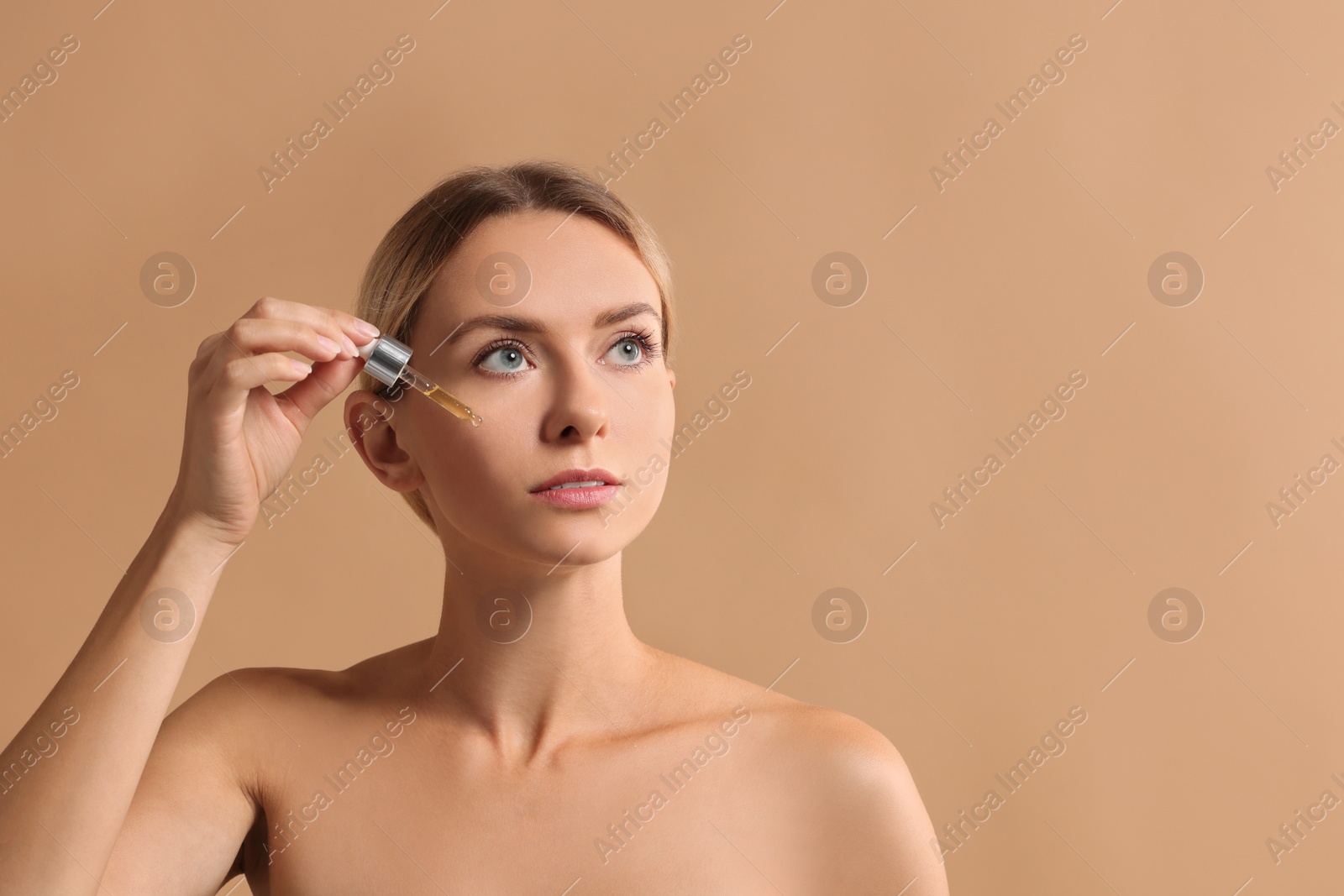 Photo of Beautiful woman applying cosmetic serum onto her face on beige background, space for text