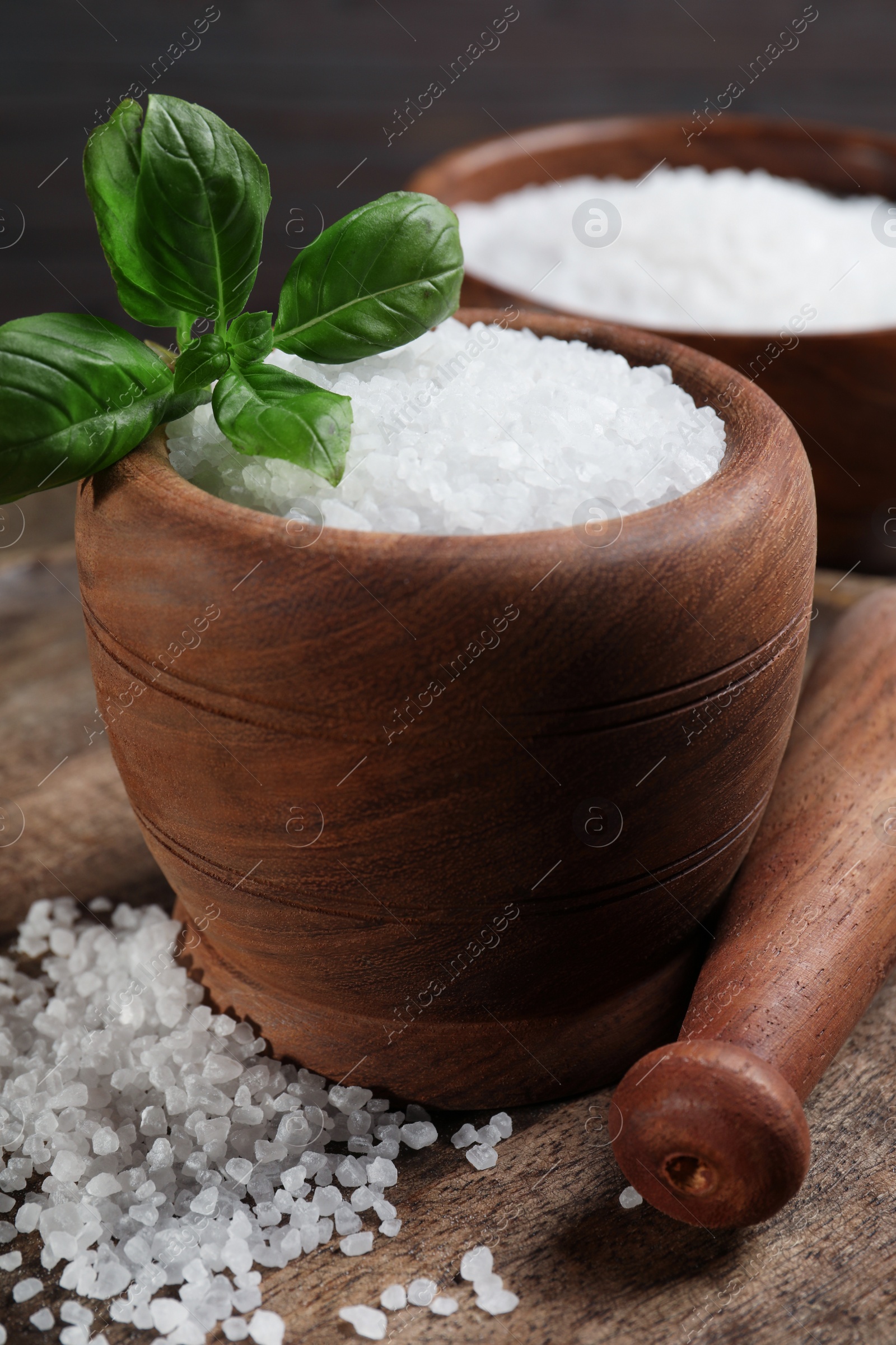 Photo of Pestle and mortar with natural sea salt on wooden table, closeup