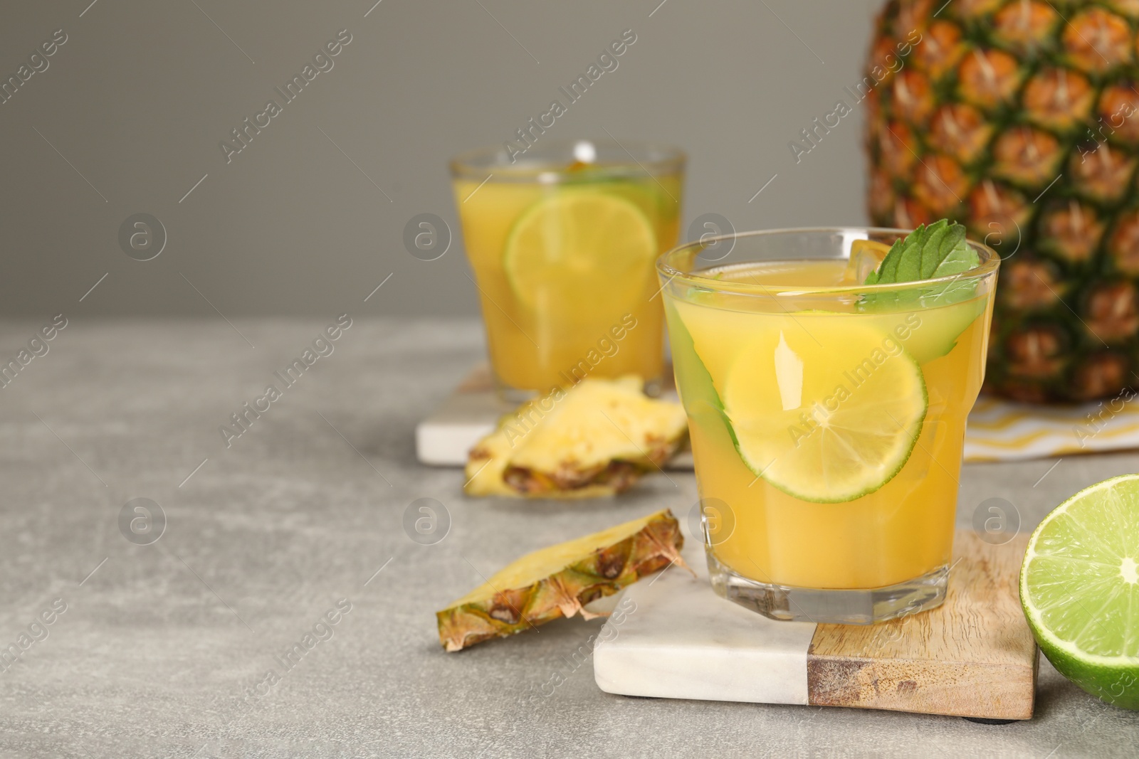 Photo of Glasses of tasty pineapple cocktail with mint and lime on light grey table. Space for text