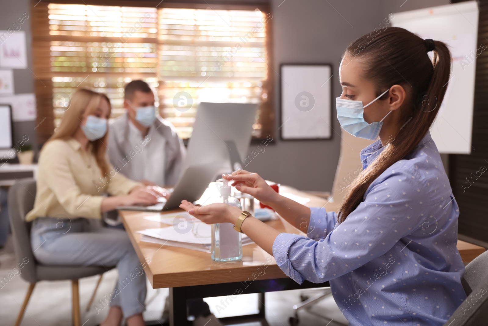 Photo of Office worker using hand sanitizer at table. Personal hygiene during COVID-19 pandemic