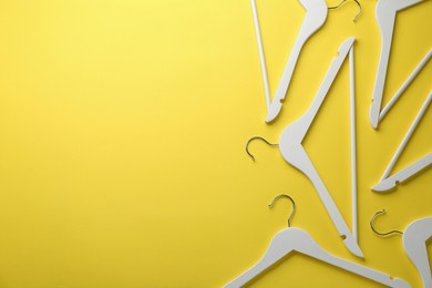 Photo of White hangers on yellow background, flat lay. Space for text