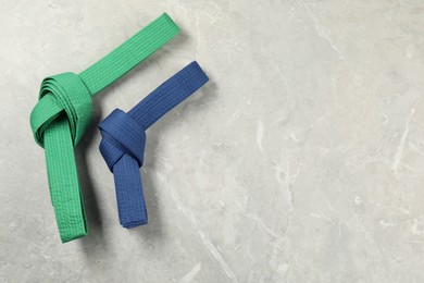 Photo of Green and blue karate belts on gray marble background, flat lay. Space for text