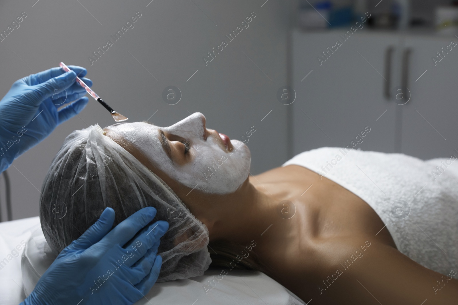 Photo of Cosmetologist applying mask on client's face in spa salon