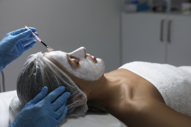 Photo of Cosmetologist applying mask on client's face in spa salon