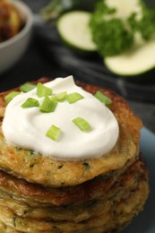 Photo of Delicious zucchini pancakes with sour cream and green onion on plate, closeup
