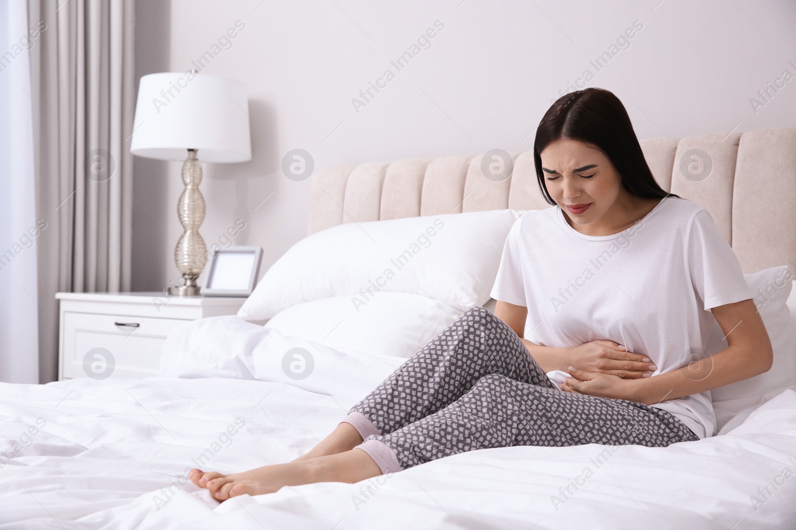 Photo of Young woman suffering from stomach ache in bedroom