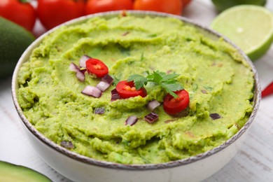 Photo of Bowl of delicious guacamole on white wooden table, closeup