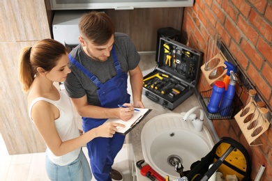 Professional plumber with client near kitchen sink