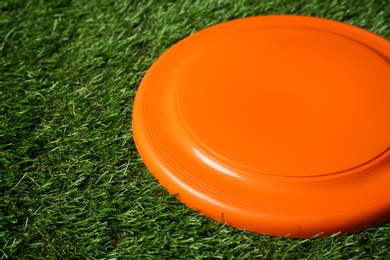 Photo of Orange plastic frisbee disk on green grass, closeup