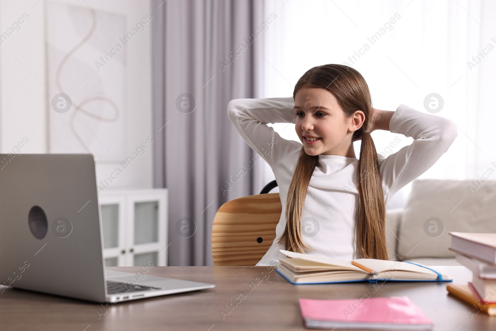 Photo of E-learning. Cute girl using laptop during online lesson at table indoors