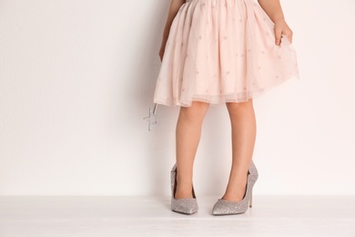 Photo of Little girl in oversized shoes near white wall with space for text, closeup on legs