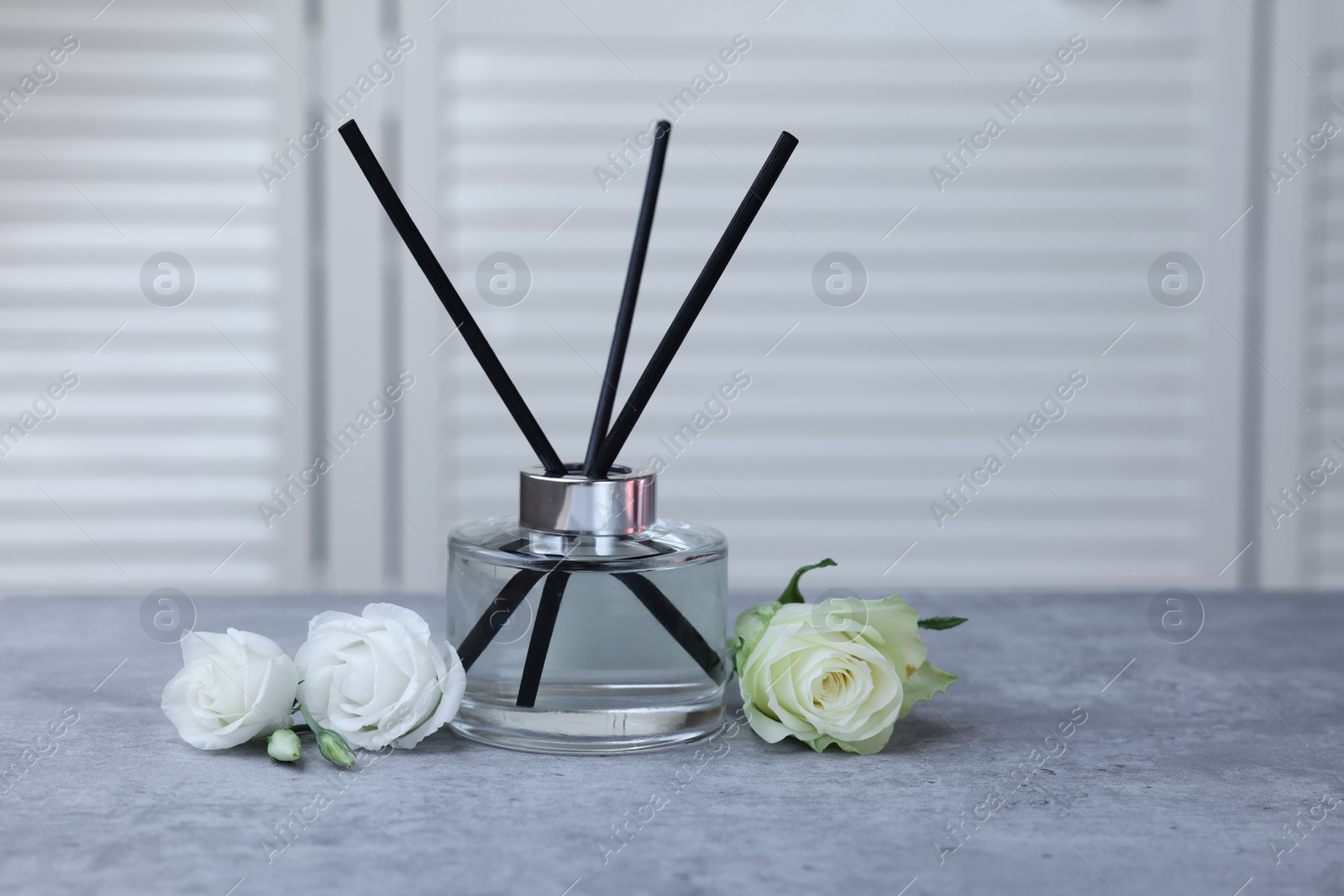 Photo of Reed air freshener and flowers on grey table indoors