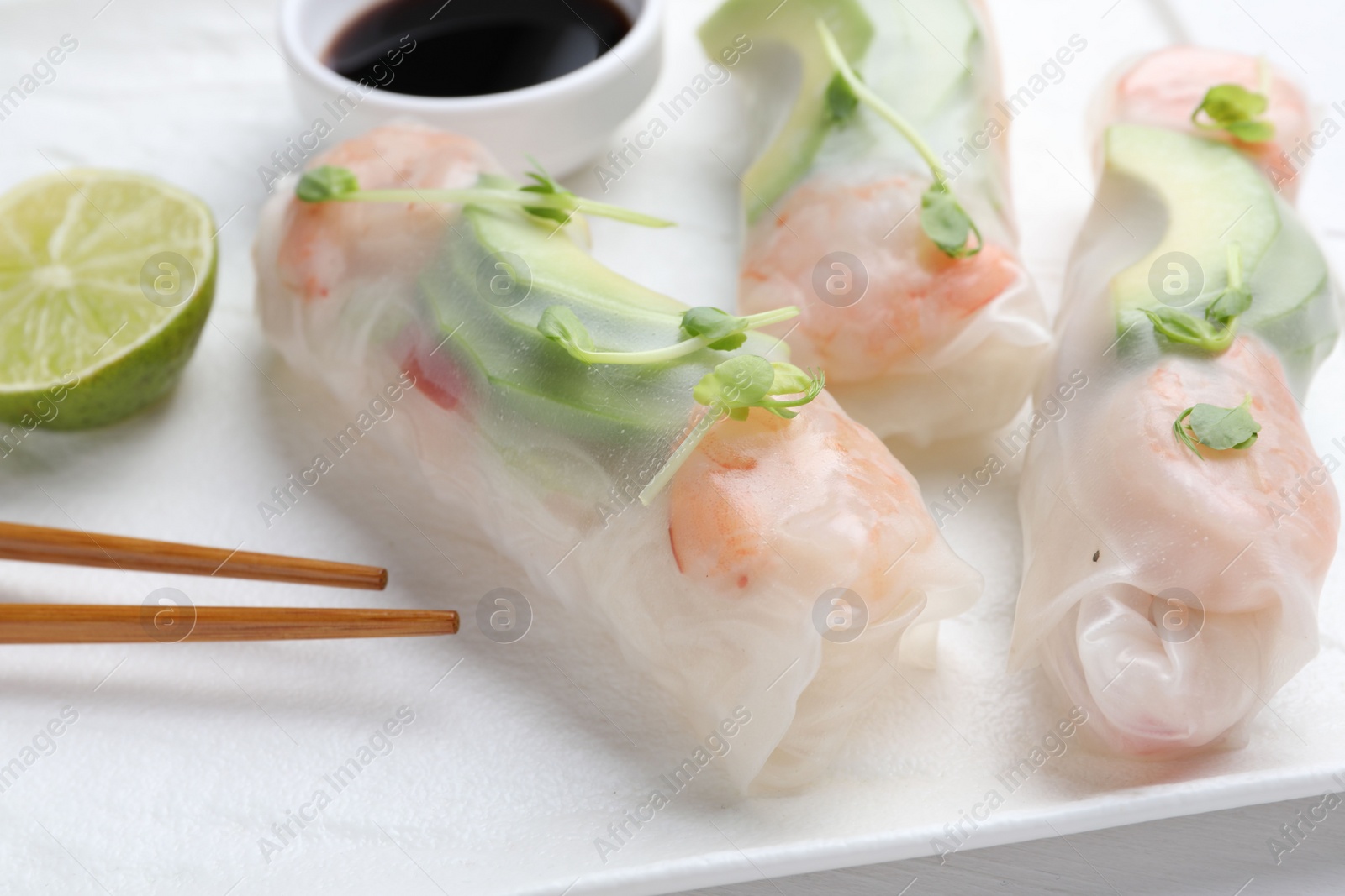 Photo of Delicious spring rolls, lime, soy sauce and chopsticks on table, closeup