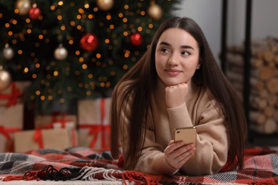 Woman with smartphone near Christmas tree indoors. Space for text