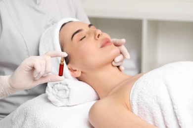 Photo of Professional cosmetologist holding skincare ampoule while working with client in clinic, closeup