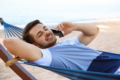 Photo of Young man talking on phone in hammock at seaside