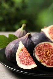 Photo of Whole and cut ripe figs on light grey table against blurred green background, closeup