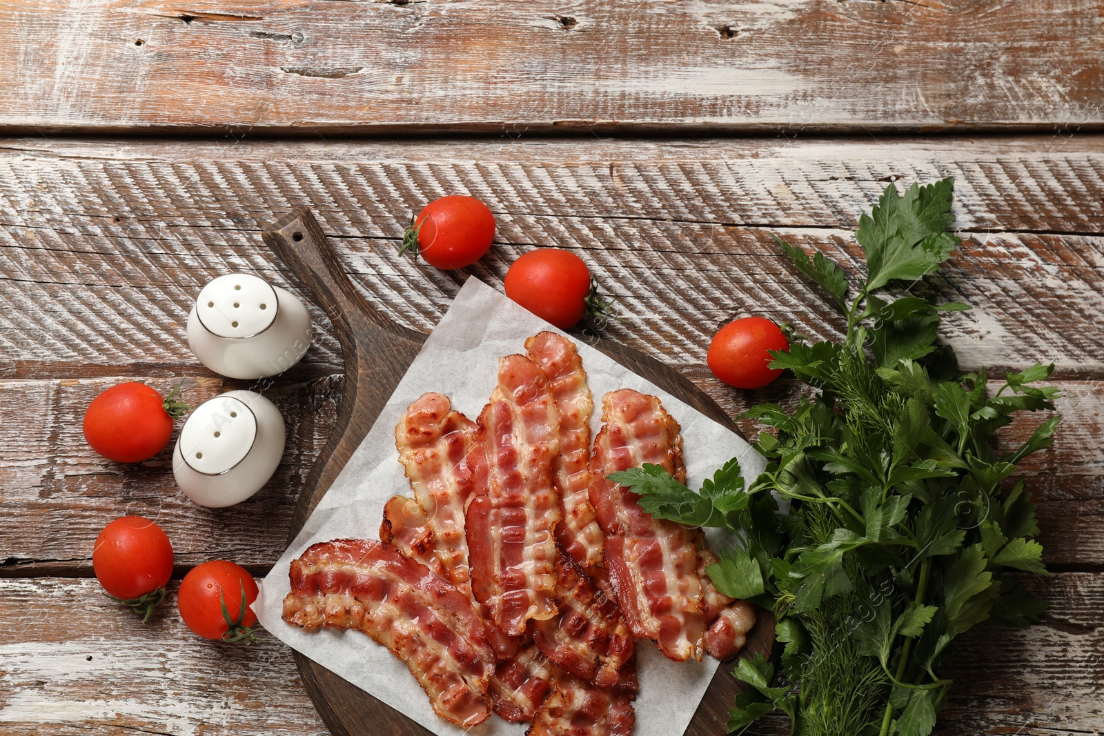 Photo of Fried bacon slices, tomatoes, parsley and spices on wooden rustic table, flat lay