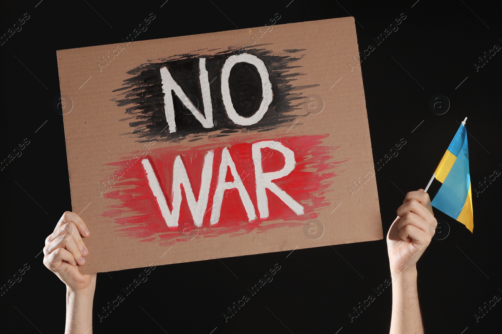 Photo of Teenage boy holding poster No War and Ukrainian flag against black background, closeup