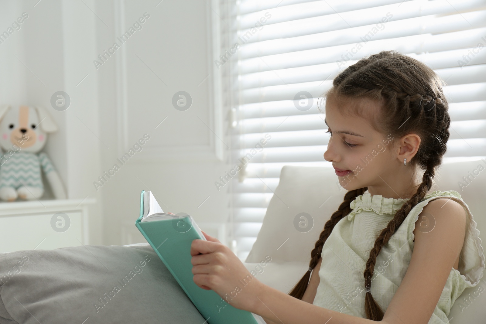 Photo of Cute little girl reading book on sofa at home