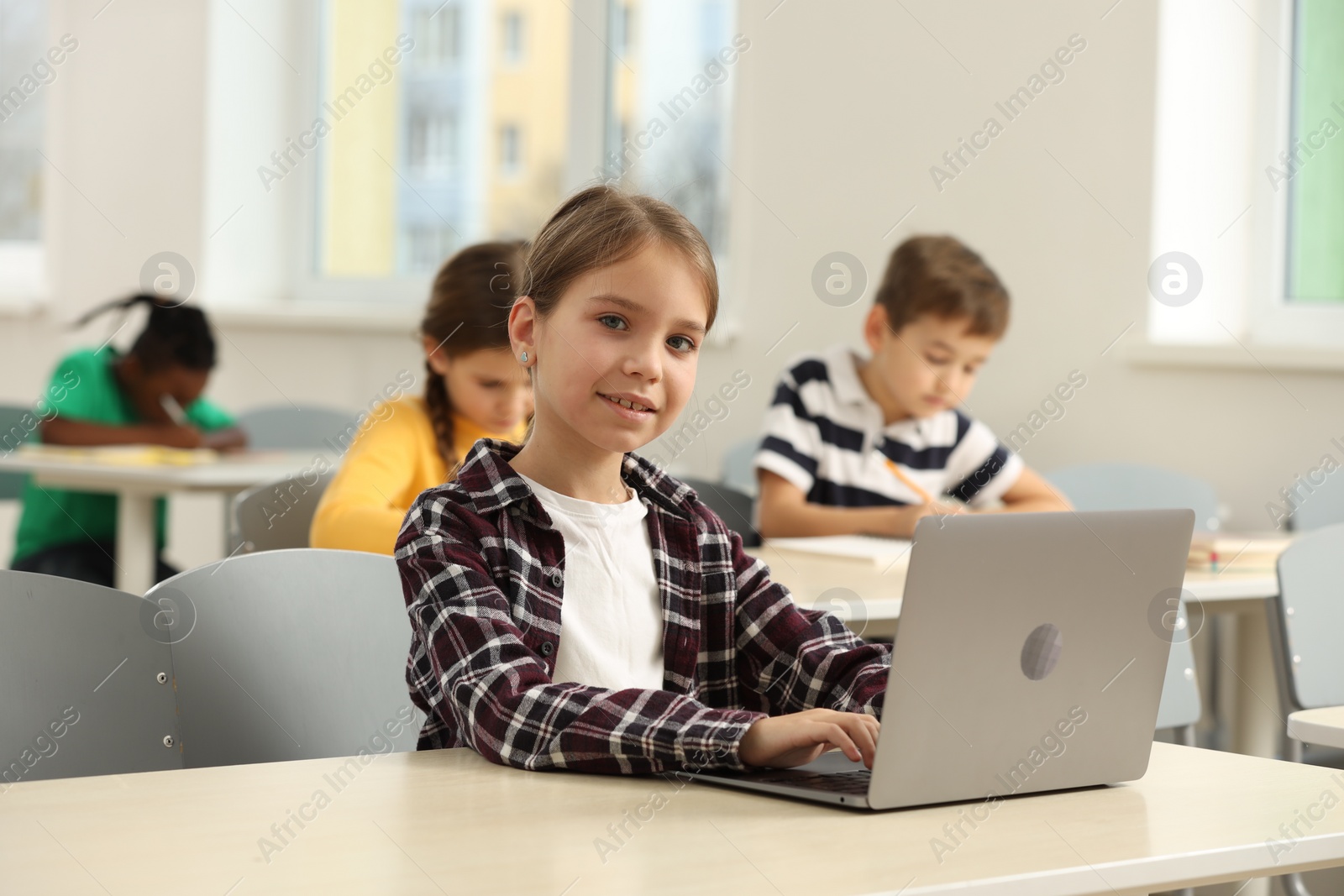 Photo of Smiling little girl with laptop studying in classroom at school