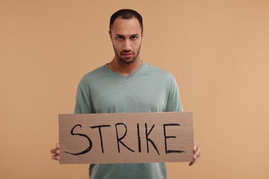 Photo of Upset man holding cardboard banner with word Strike on beige background