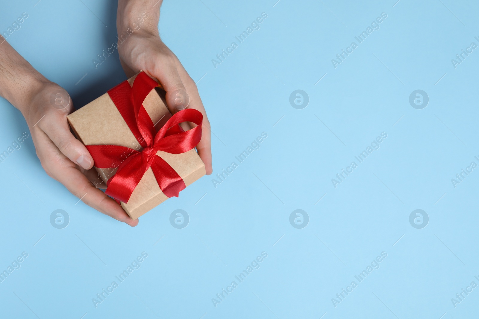 Photo of Man holding gift box with red bow on light blue background, top view. Space for text