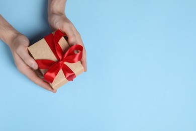 Photo of Man holding gift box with red bow on light blue background, top view. Space for text