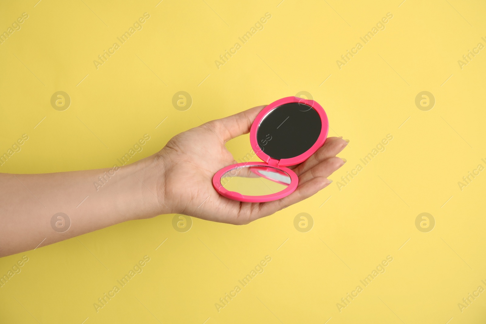 Photo of Woman holding pink cosmetic pocket mirror on yellow background, closeup