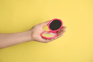 Woman holding pink cosmetic pocket mirror on yellow background, closeup