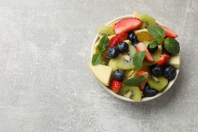 Photo of Tasty fruit salad in bowl on gray textured table, top view. Space for text