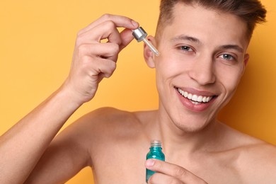 Photo of Handsome man applying serum onto his face on orange background