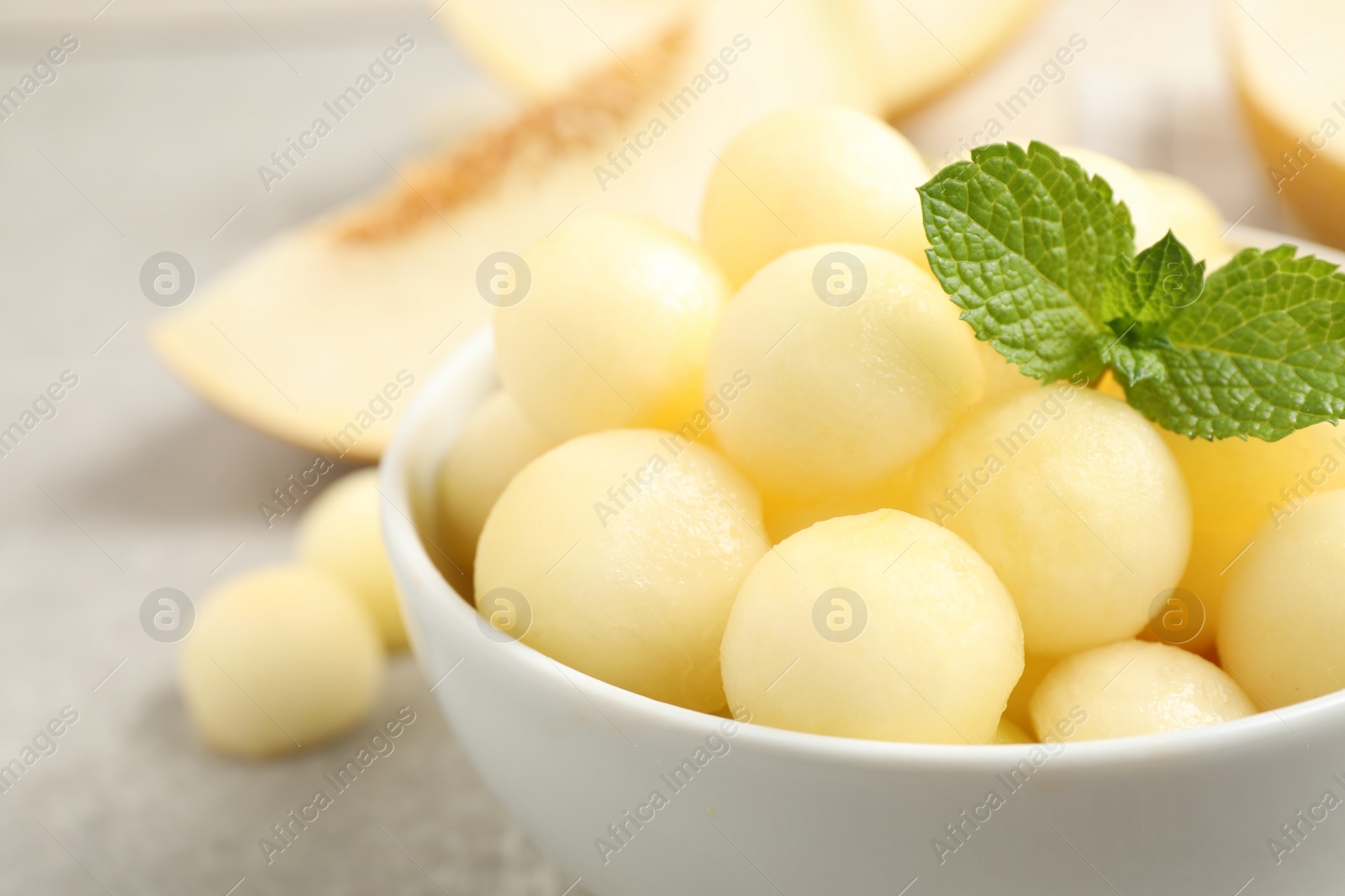 Photo of Melon balls and mint in bowl on light grey table, closeup. Space for text