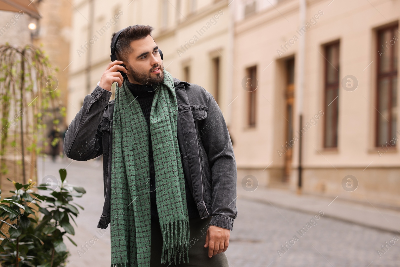 Photo of Smiling man in warm scarf listening to music outdoors. Space for text