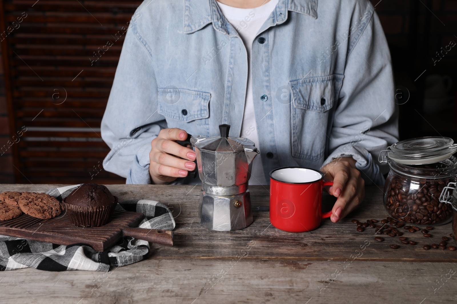 Photo of Brewing coffee. Woman with moka pot, cup, cookies and muffin at wooden table, closeup