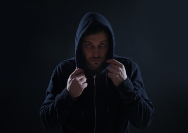 Mysterious man in hoodie on dark background. Dangerous criminal