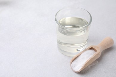 Vinegar in glass, baking soda and wooden scoop on light table, space for text