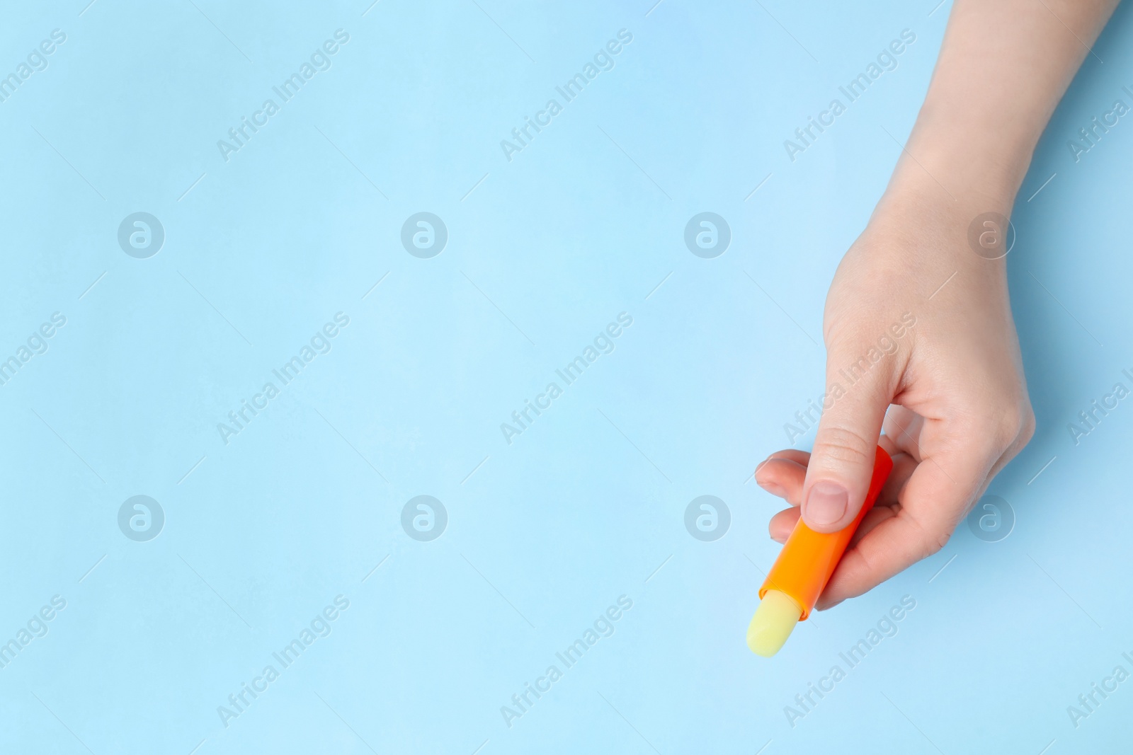 Photo of Woman holding hygienic lipstick on light blue background, top view. Space for text