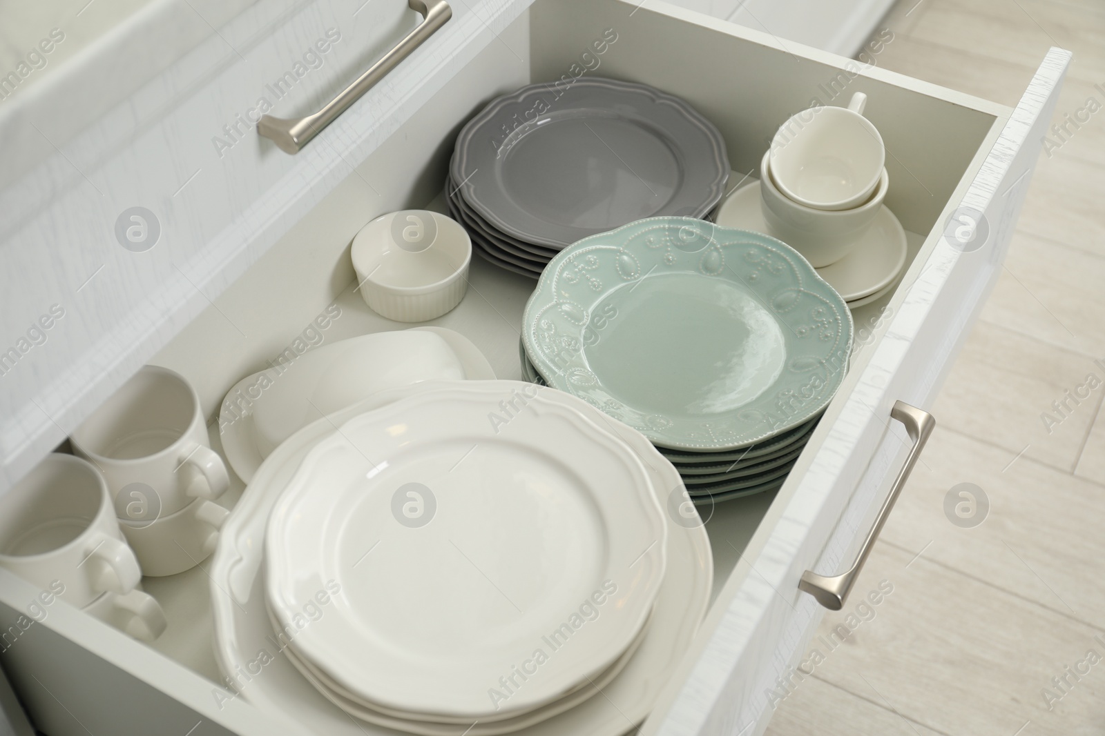 Photo of Clean plates, cups, butter dish and bowl in drawer indoors