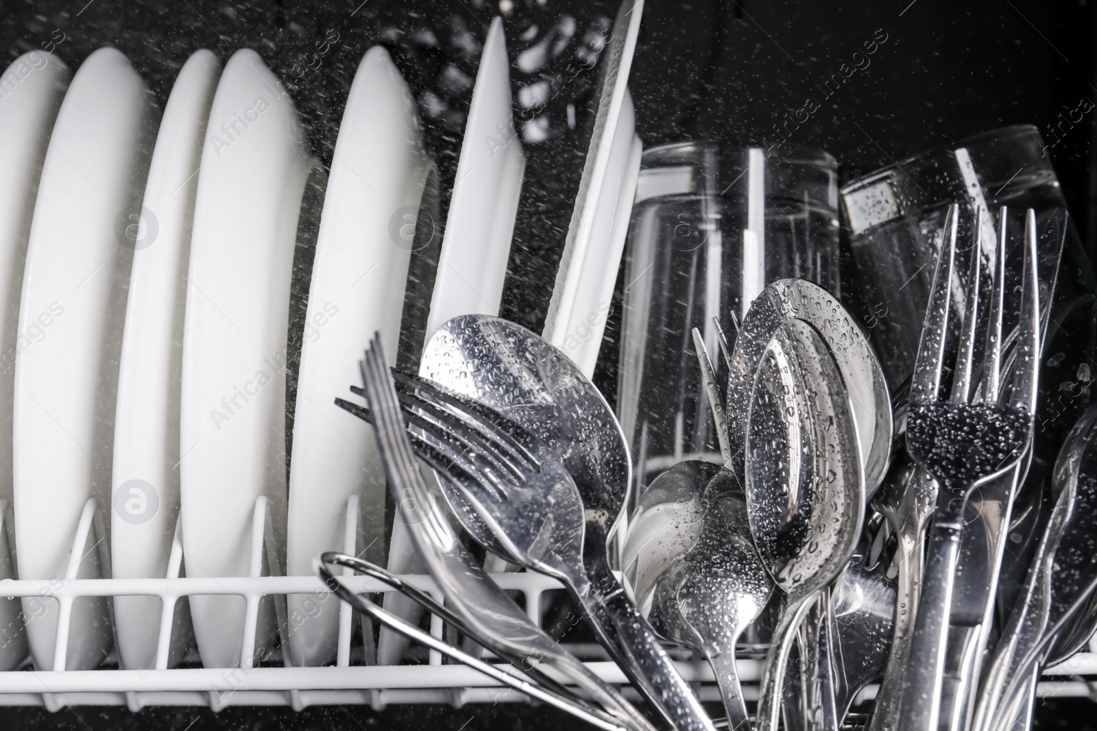 Photo of Clean wet plates and cutlery in dishwasher, closeup