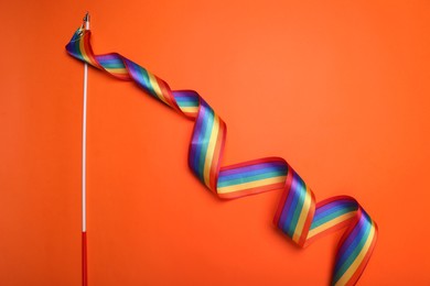 Photo of Stick with rainbow ribbon on orange background, top view. LGBT pride