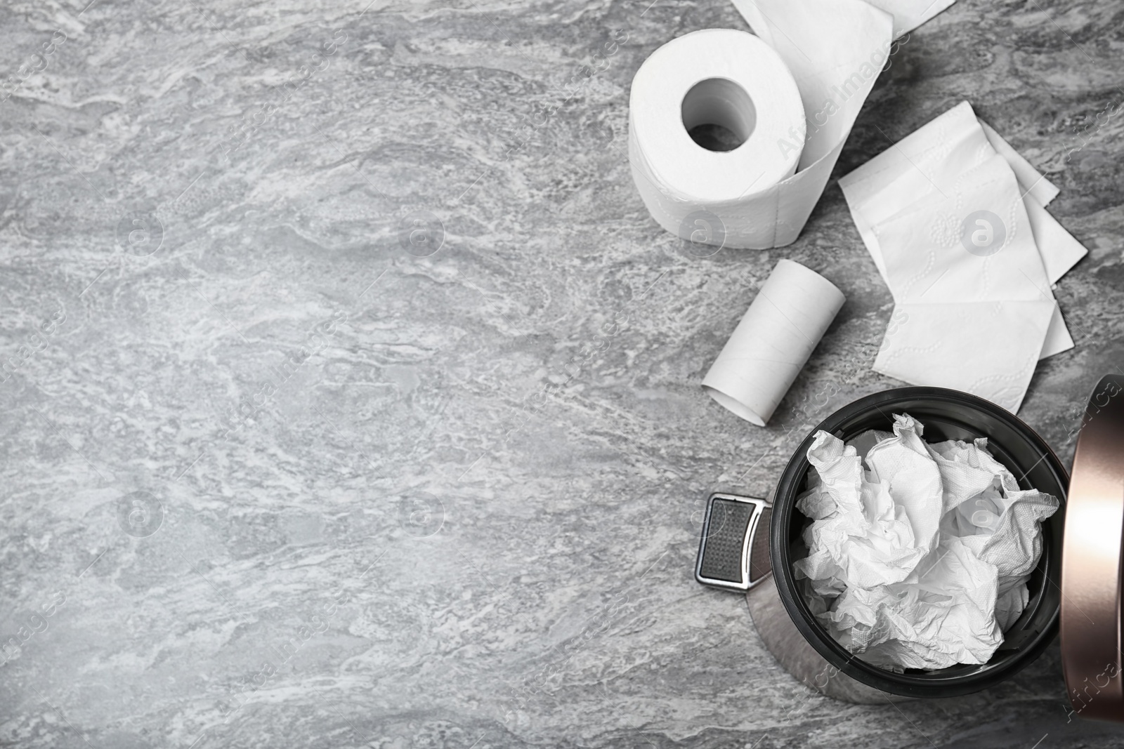 Photo of Trash bin with used toilet paper and new roll on grey background, top view. Space for text