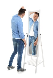 Photo of Young man looking at himself in mirror on white background