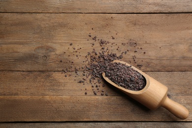 Photo of Black salt in scoop on wooden table, top view. Space for text